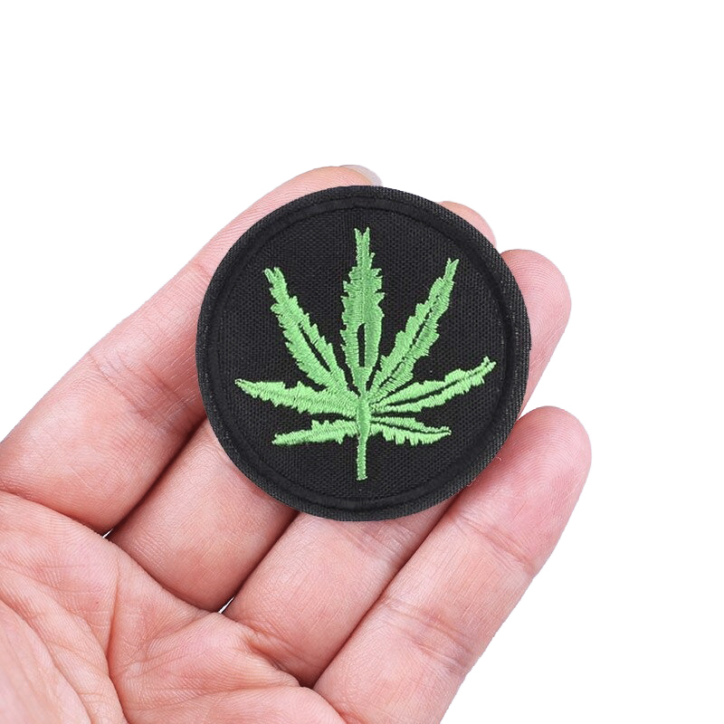 Hand holding a round ganja leaf print fusible patch, perfect for alternative fashion accessories on clothes.
