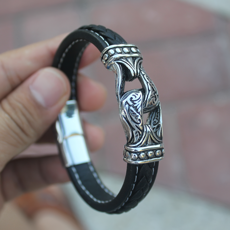 Hand holding a gothic style stainless steel and leather bracelet, showcasing intricate designs and high-quality craftsmanship.