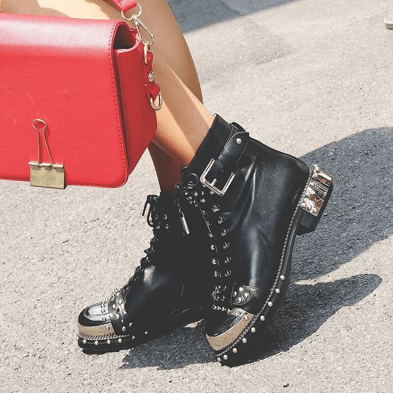 Stylish women's punk rock leather ankle boots with rivets and chains, paired with a chic red handbag.