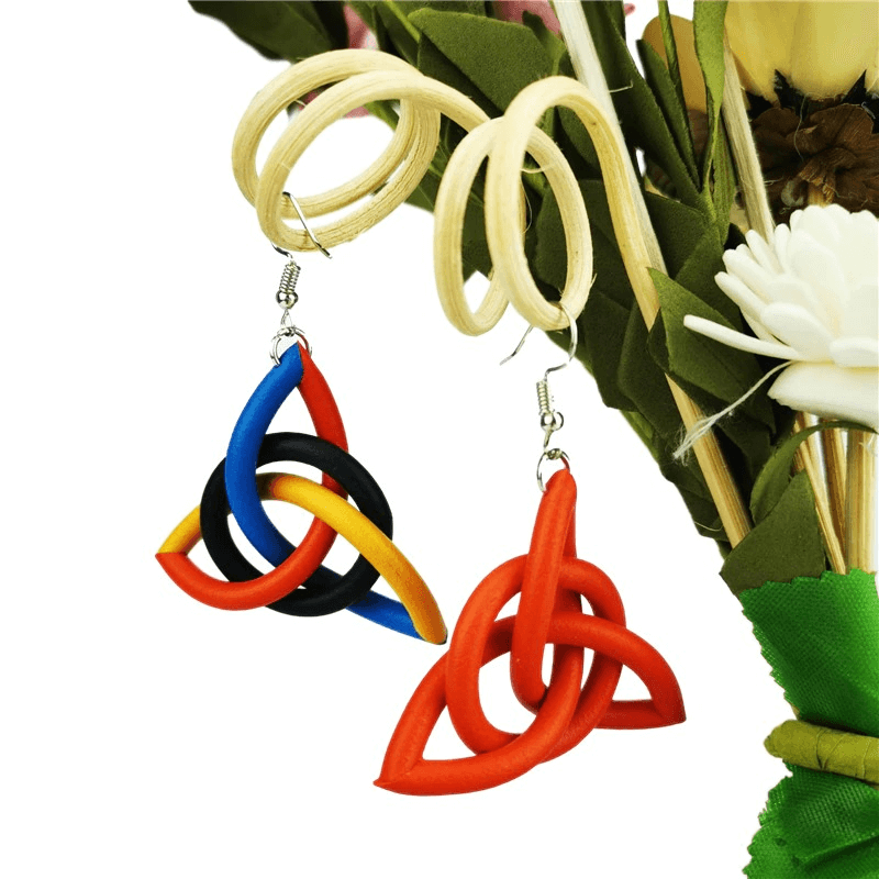 Colorful geometric drop earrings in red, blue, black, and yellow, handmade ethnic accessories on a vibrant floral background.