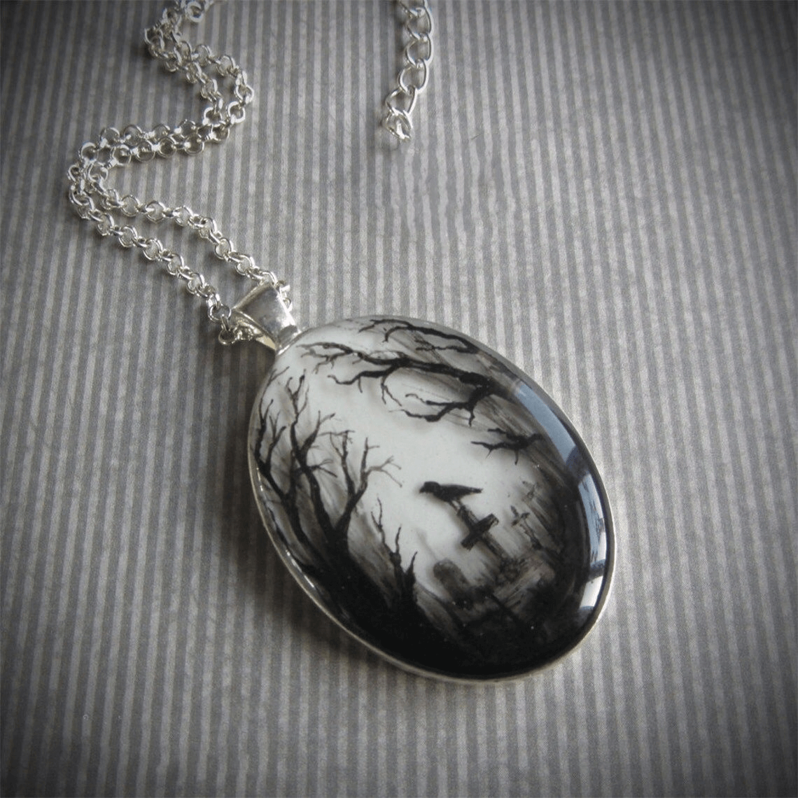 Hand painted oval pendant featuring a graveyard scene with trees and a crow, perfect for gothic style enthusiasts.