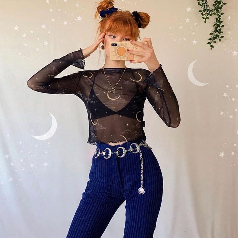 Stylish woman in a sheer top and high-waisted pants, showcasing a gothic moon belt and playful hairstyle.