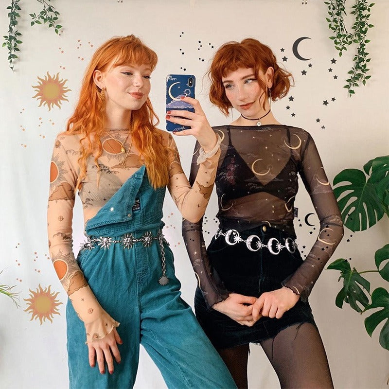 Two women showcasing trendy gothic outfits with moon motifs, featuring sheer tops and stylish chain belts.
