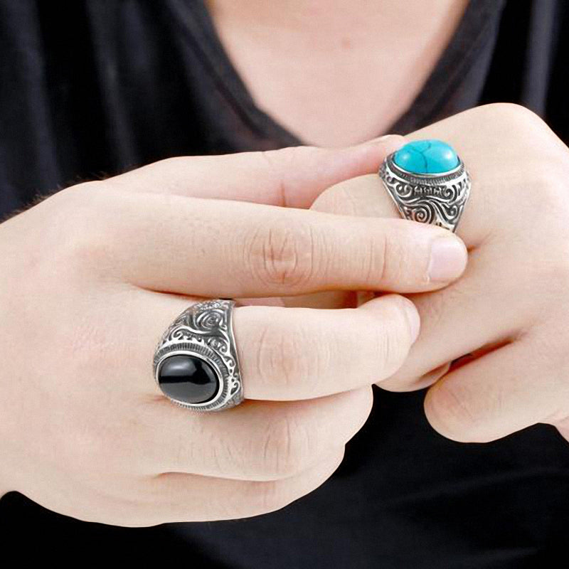 Person wearing two distinctive rings: a turquoise stone ring and a black stone ring, showcasing alternative Gothic style.