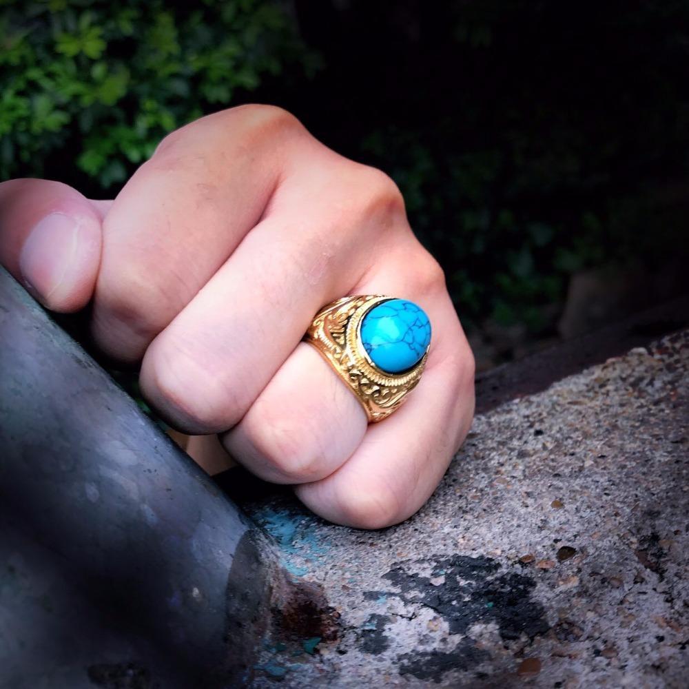 A person's hand with a gold ring featuring a large turquoise stone, set against a rustic backdrop.