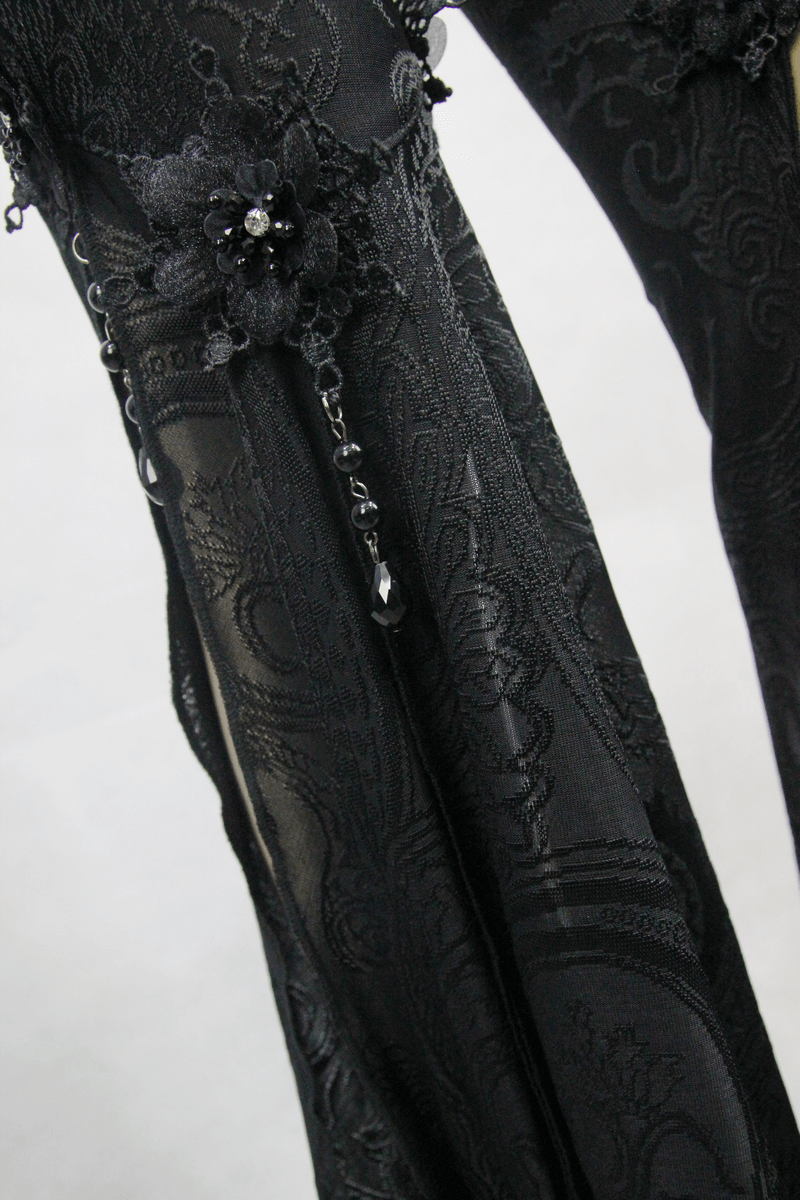 Close-up of black gothic flare pants with intricate lace details and decorative pendants.