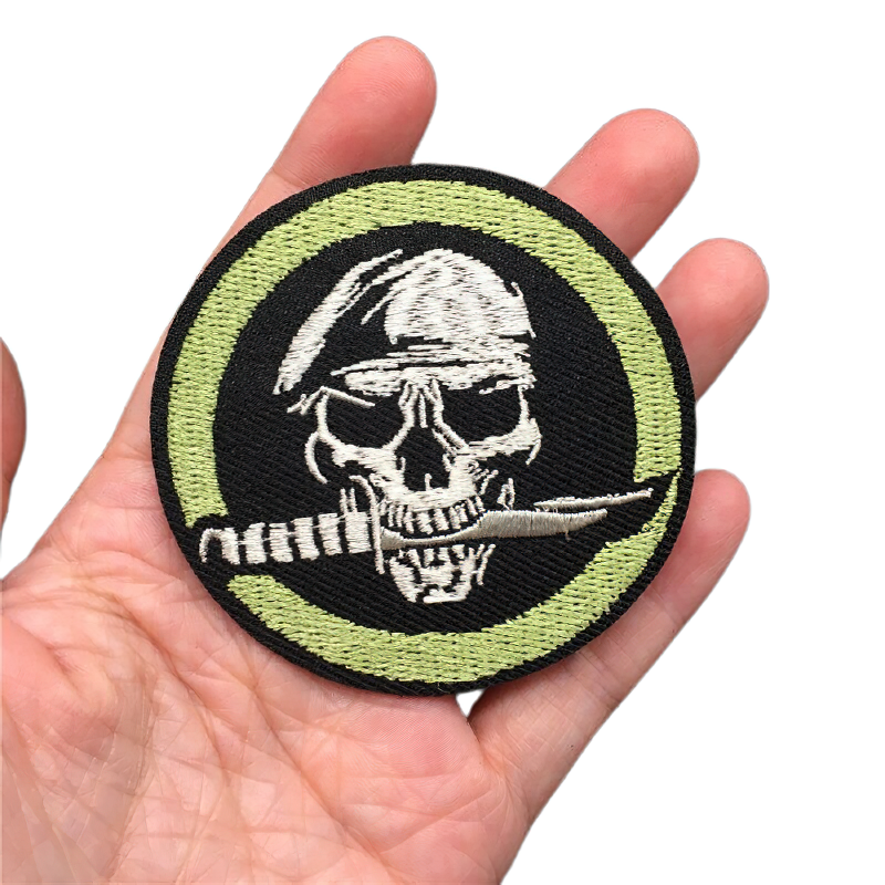 Gothic skull patch in hand, featuring a knife in teeth and circular design, perfect unisex fashion accessory.