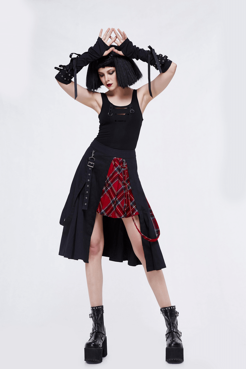 Gothic punk woman wearing an asymmetrical black plaid skirt and black top, posing confidently in edgy fashion.
