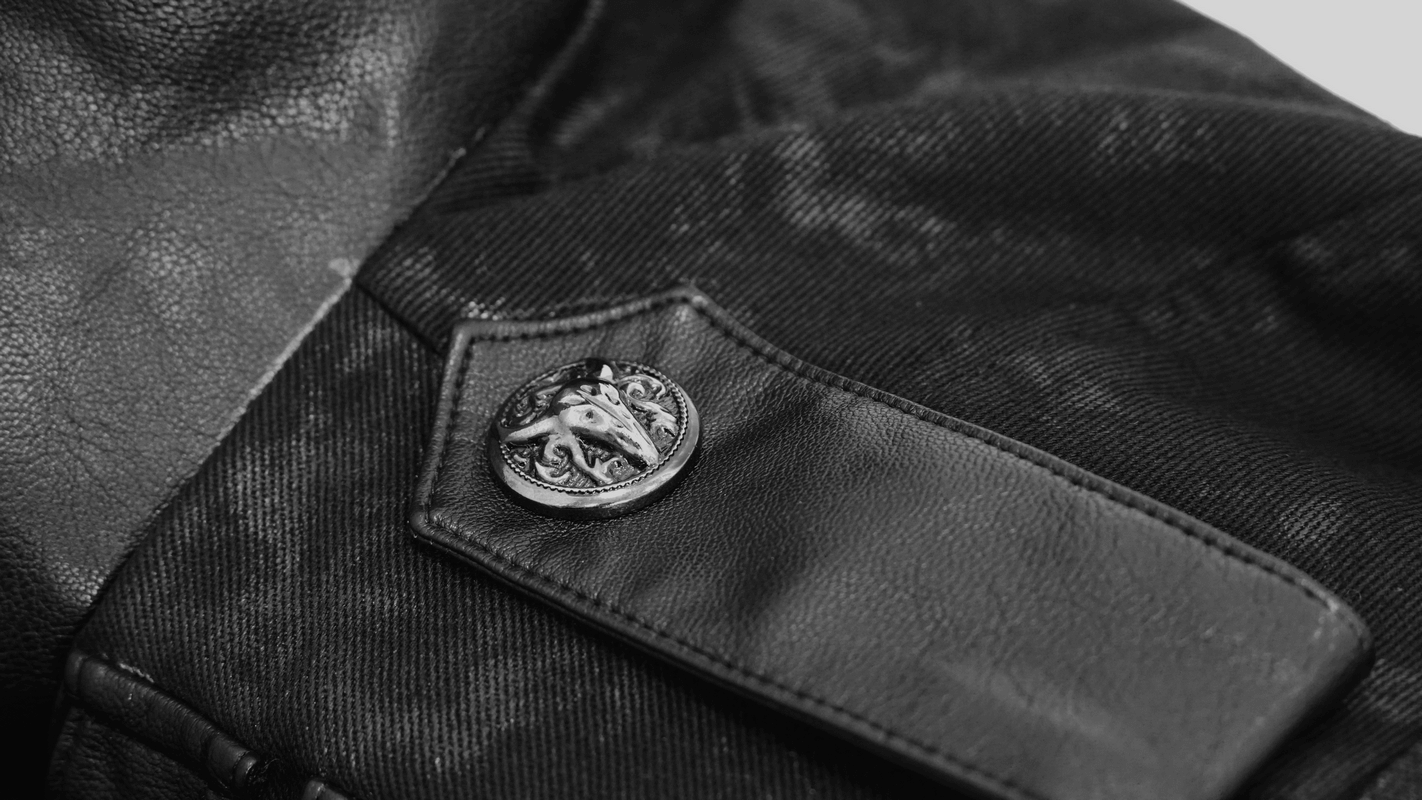 Close-up of a black fabric with a vintage-style metal button emblem on a men's gothic punk trench coat.