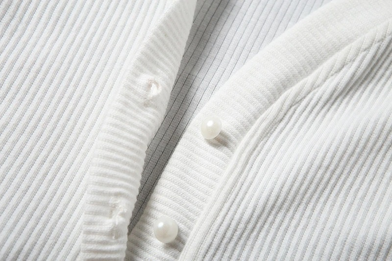 Close-up of a white ribbed cardigan with pearl buttons, showcasing elegant texture and style.