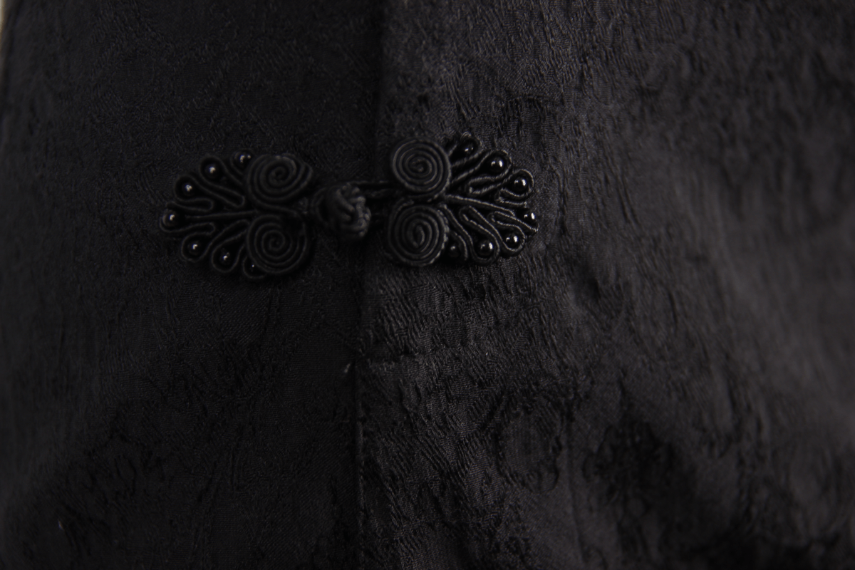 Close-up of elegant black fabric with intricate lace tassel detail and stylish button accent.