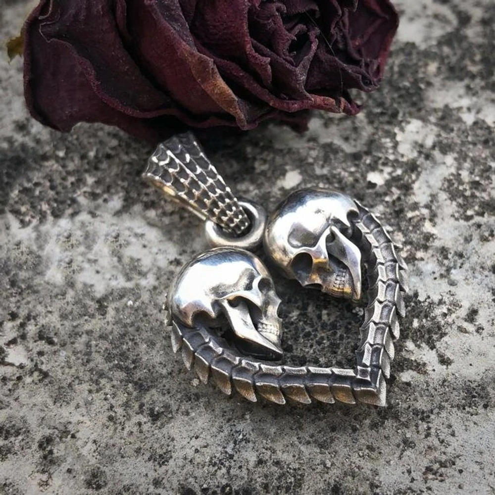 Gothic stainless steel double skull heart necklace pendant resting beside a dried rose.