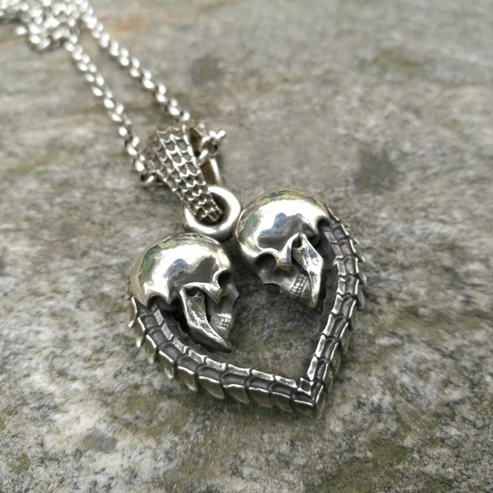 Gothic stainless steel double skull heart necklace pendant on a textured background.