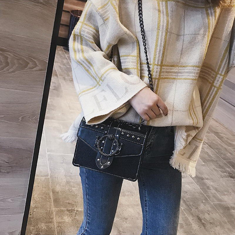 Gothic style women's small square bag with chain and rivets, paired with a stylish plaid sweater and jeans.