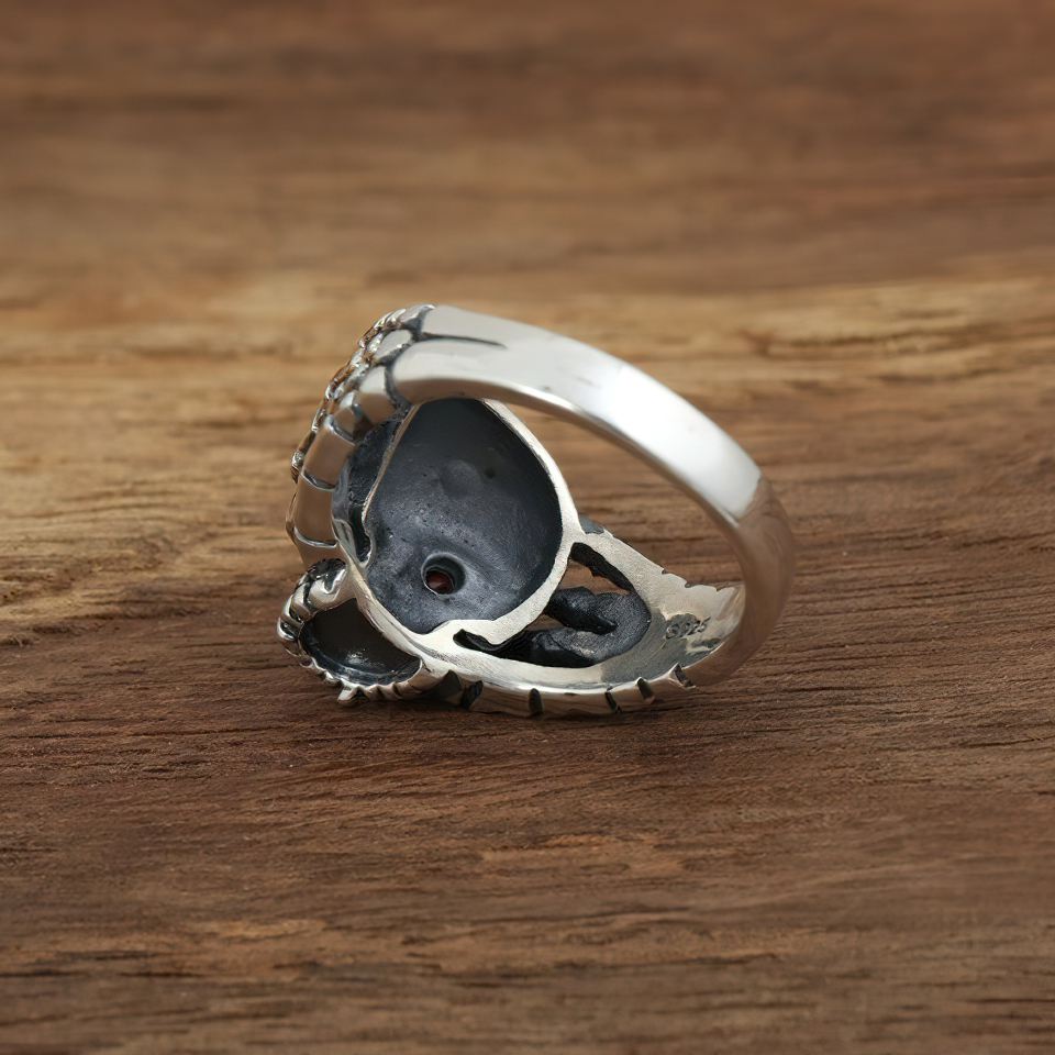 Sterling silver gothic ring featuring a skull design with red eye detail on a wooden surface.