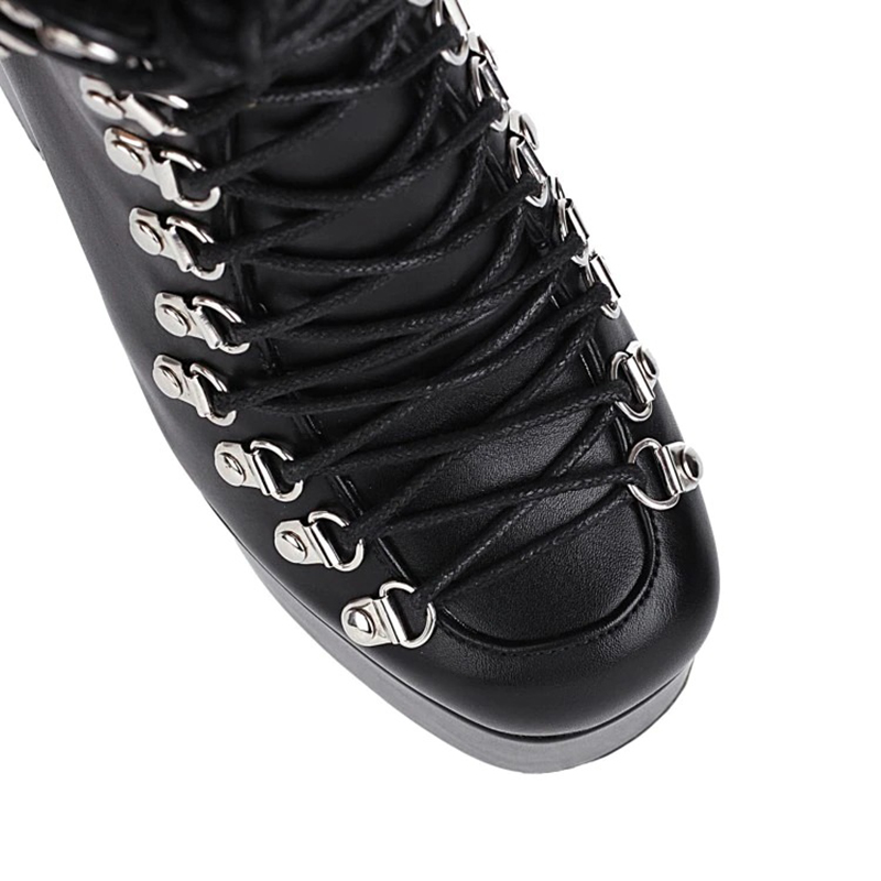 Close-up of gothic women's patent leather short boots with silver eyelet laces and sleek black design.