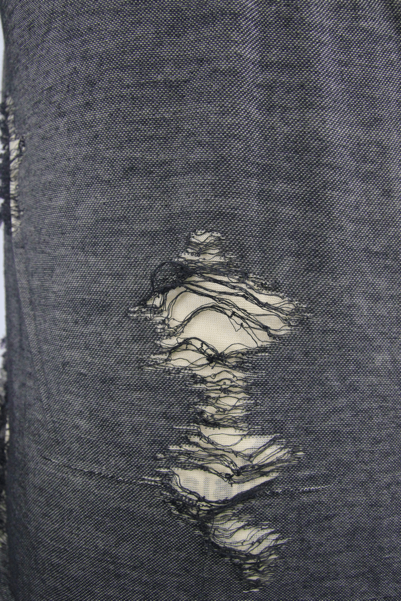 Close-up of distressed fabric with irregular holes, showcasing grunge style detail and texture.