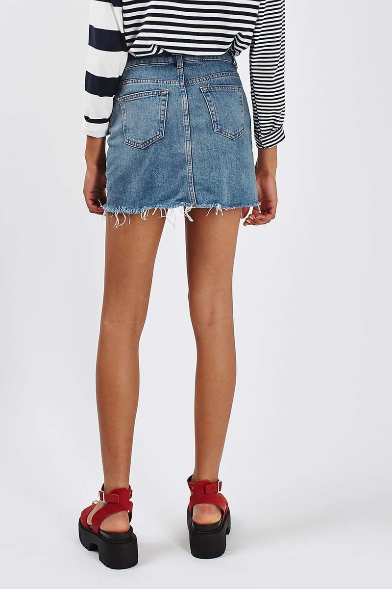 Back view of a grunge style high waist denim blue mini skirt with pockets, paired with a striped shirt.