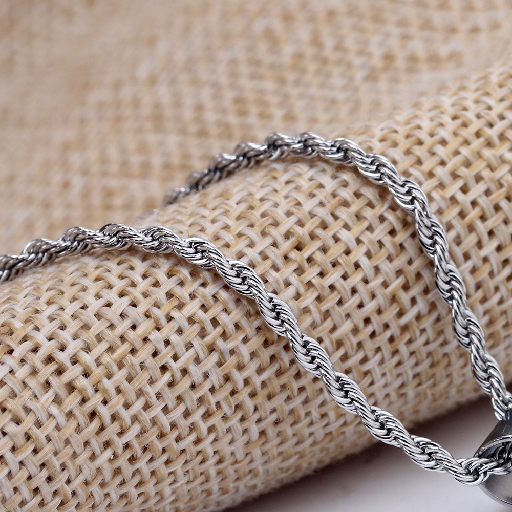 Twisted stainless steel chain necklace on a textured fabric background, perfect for rock and punk fashion.