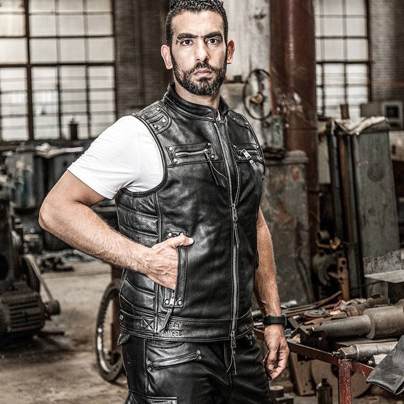 Stylish man wearing a black leather motorcycle biker vest, showcasing a bold biker fashion look in an industrial setting.