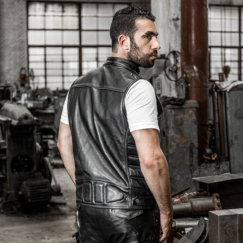 Man showcasing a men's genuine leather biker vest in a workshop setting, exuding a cool, edgy style.