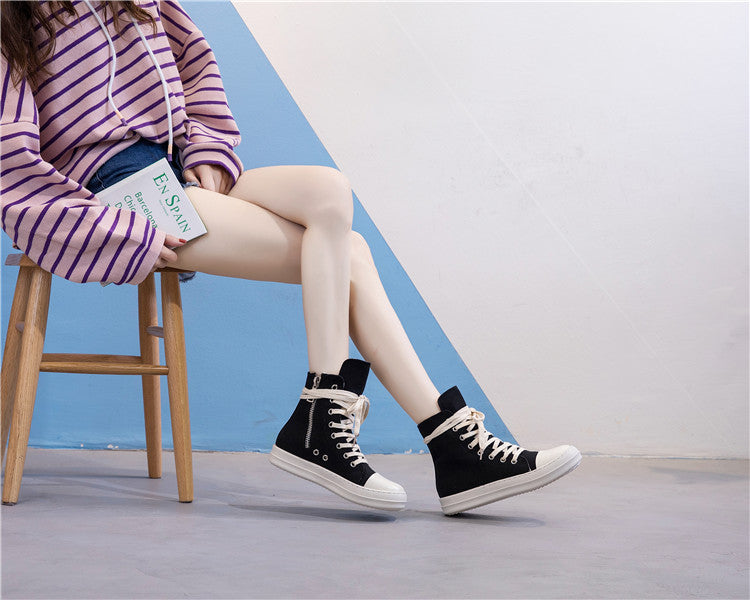 Stylish female legs wearing black high top sneakers with a white sole and casual outfit sitting on a wooden chair.