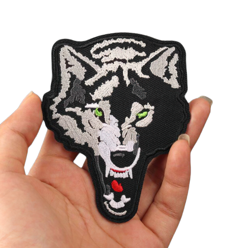 Angry green-eyed wolf embroidered iron-on patch held in hand, trendy rock style accessory for clothing.