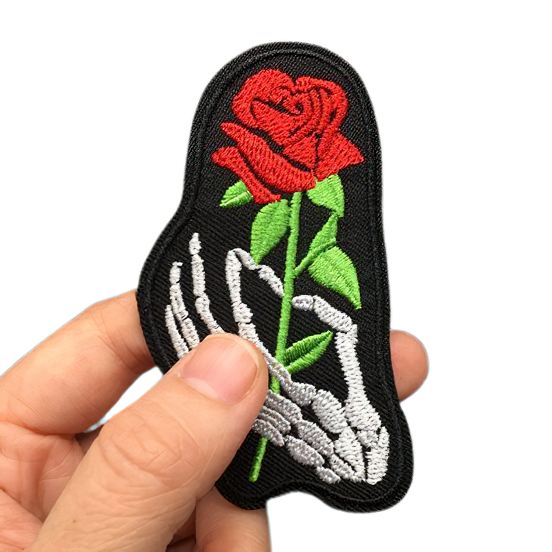 Stylish iron-on patch featuring a skeleton hand holding a vibrant rose, perfect for gothic clothing.