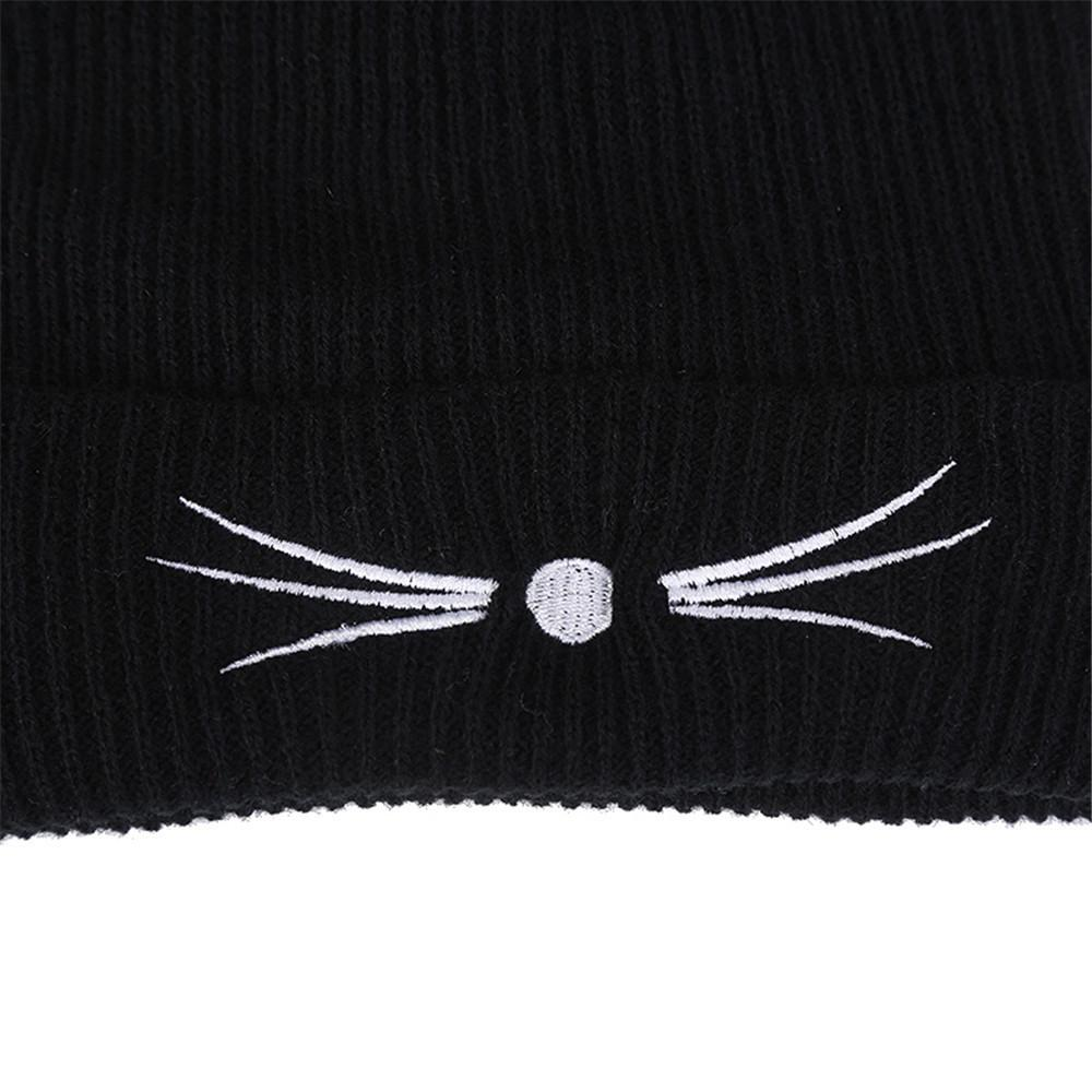 Close-up of a black knitted beanie featuring white cat whiskers and a cute nose design, perfect for trendy winter fashion.
