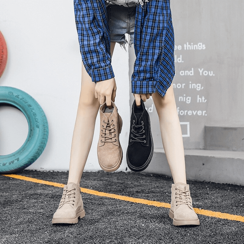 Woman holding two pairs of stylish suede ankle boots in black and beige, showcasing trendy platform design.