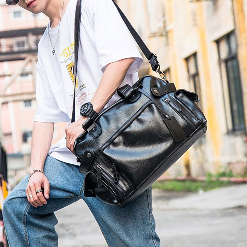 Stylish men's black leather messenger bag complementing a casual outfit, perfect for travel and gothic style.