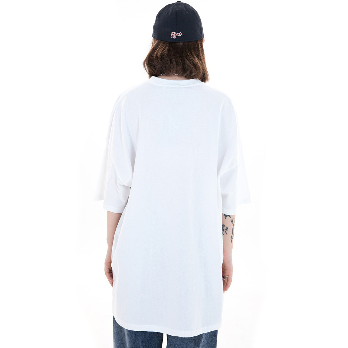 Back view of a model wearing a baggy white Lightning Punk Tee, paired with a navy cap, showcasing casual streetwear style.