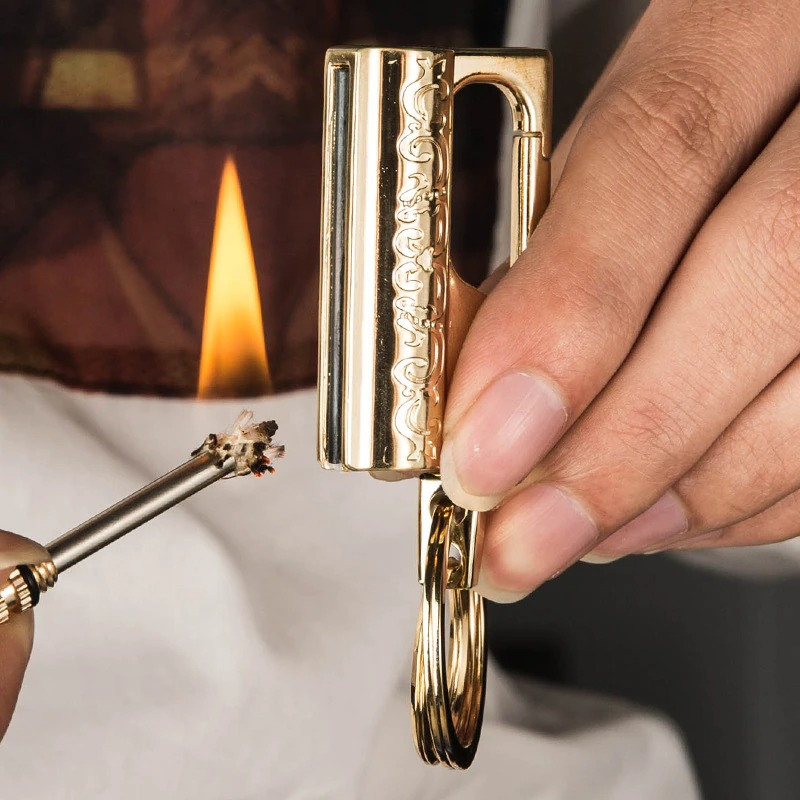 Elegant multifunction keychain lighter in gold being used to light a match, showcasing style and functionality.