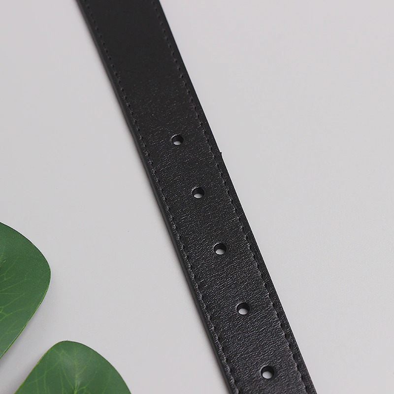 Close-up of a luxury wide black leather belt showing holes for adjustable fit, paired with green leaves.