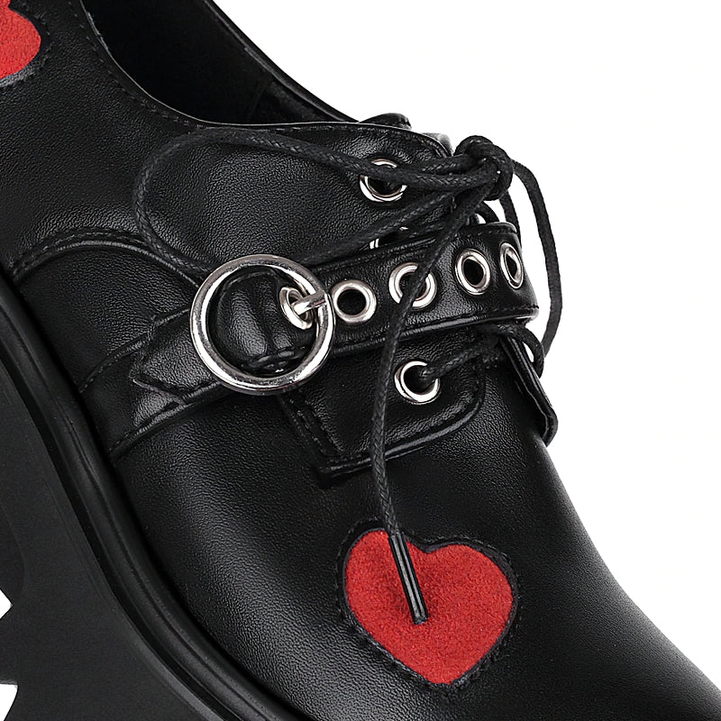 Close-up of black chunky pumps featuring heart-shaped decor, perfect for goth or punk fashion lovers.