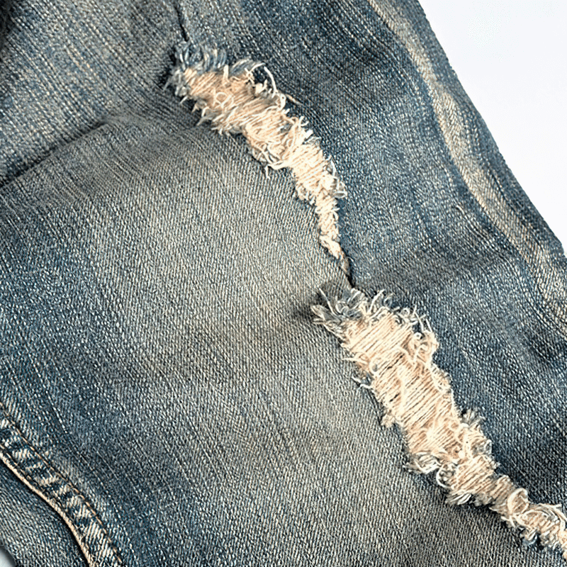 Close-up of ripped denim jeans showing distressed details and stylish embroidery for men.