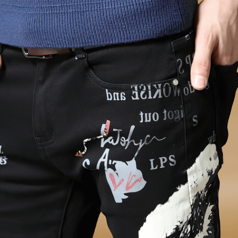 Close-up of men's black denim graffiti pants featuring unique designs and pockets in alternative fashion style.