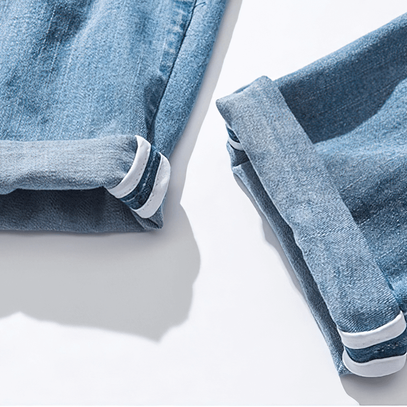 Close-up of rolled cuffs on stylish loose denim pants in light blue, showcasing casual fashion details.