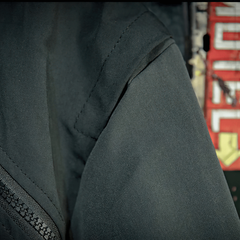 Close-up of the shoulder seam on a male patchwork stand collar jacket with zipper details.