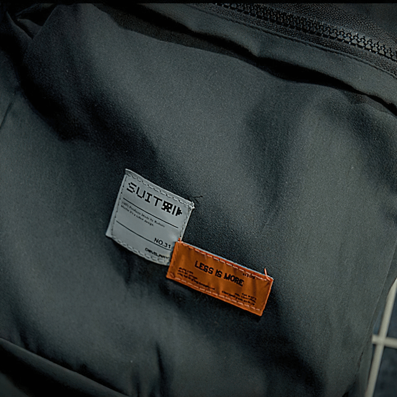 Close-up of patchwork labels on a trendy black men's jacket featuring 'LESS IS MORE' tag.