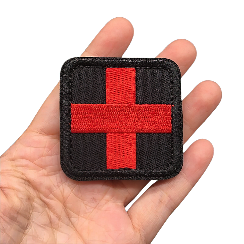 Unisex tactical medical patch, black background with red cross design, stylish military accessory in hand.