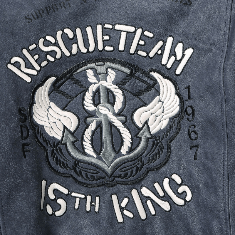 Close-up of an embroidered emblem featuring wings, anchor, and text 'RESCUETEAM 15TH KING 1967' on a leather jacket.
