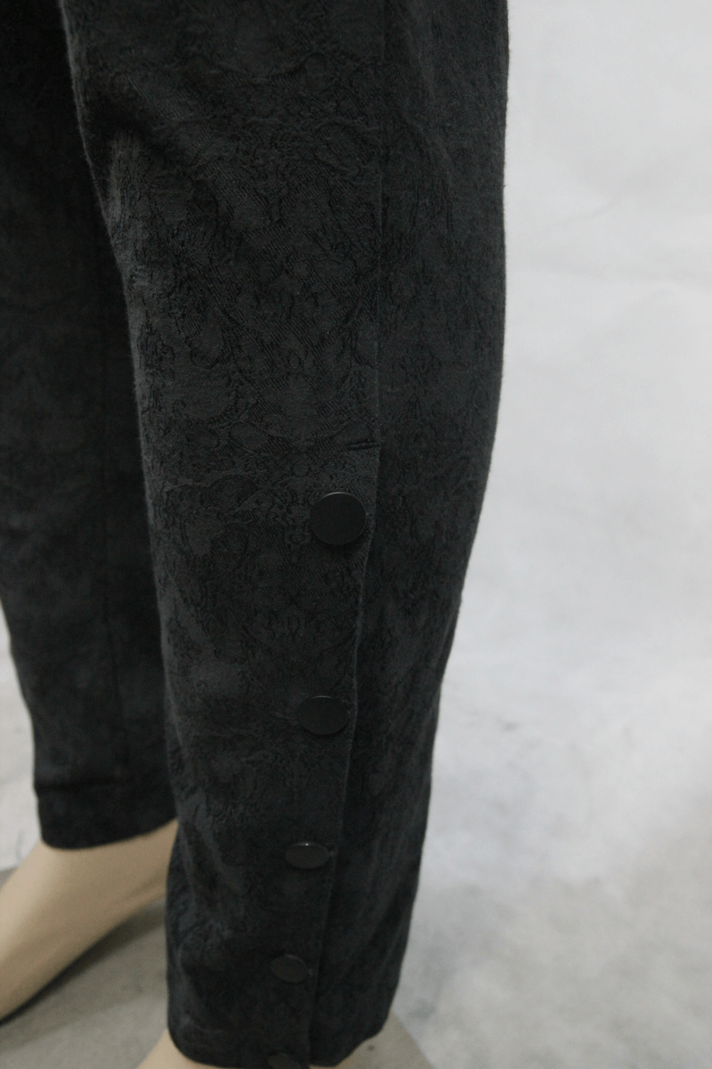 Close-up of men's goth baggy black trousers featuring delicate pattern and stylish buttons.