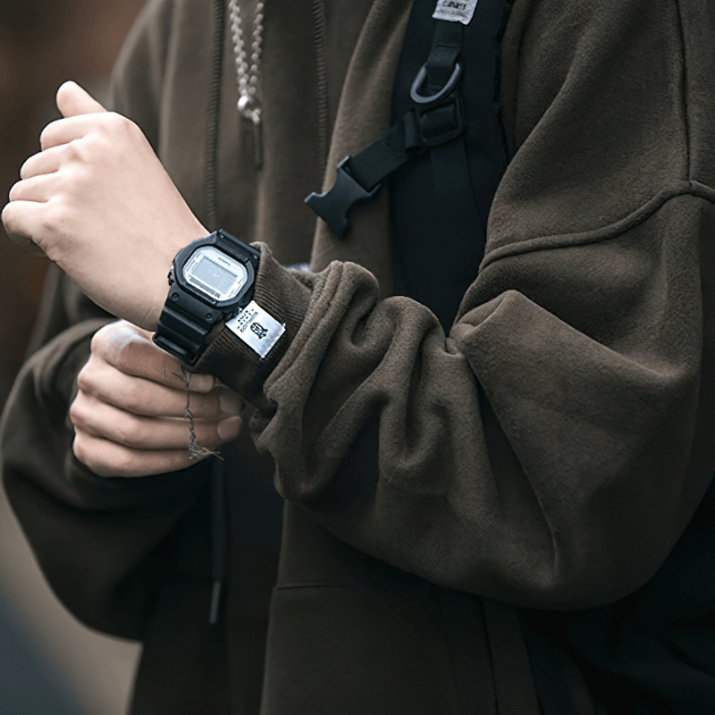 Close-up of a person wearing a brown fleece hoodie and a stylish black watch, embodying alternative fashion.