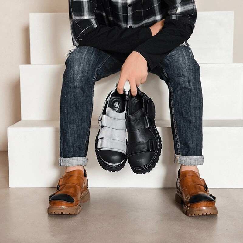 Man holding black and gray punk rock genuine leather shoes while sitting on stairs.