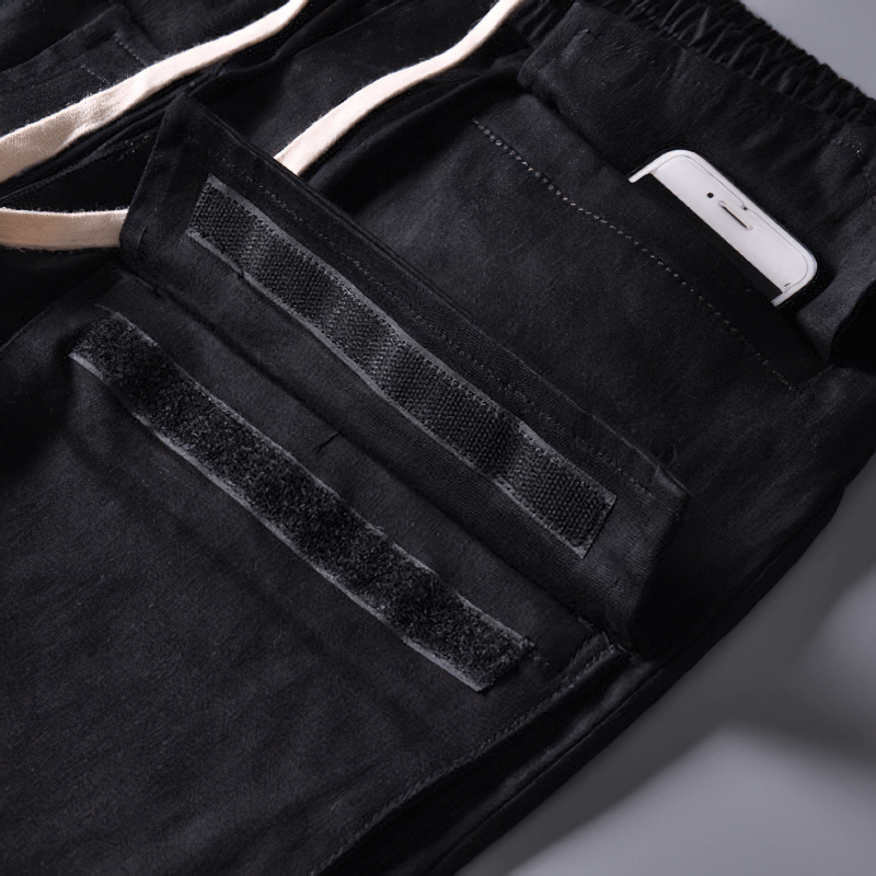Close-up of multi-pocket black cargo joggers with phone in pocket, designed for stylish and functional wear.