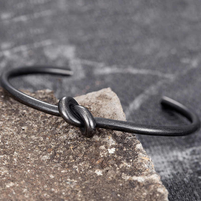 Men's aesthetic stainless steel bracelet with a unique knot design on a textured surface.