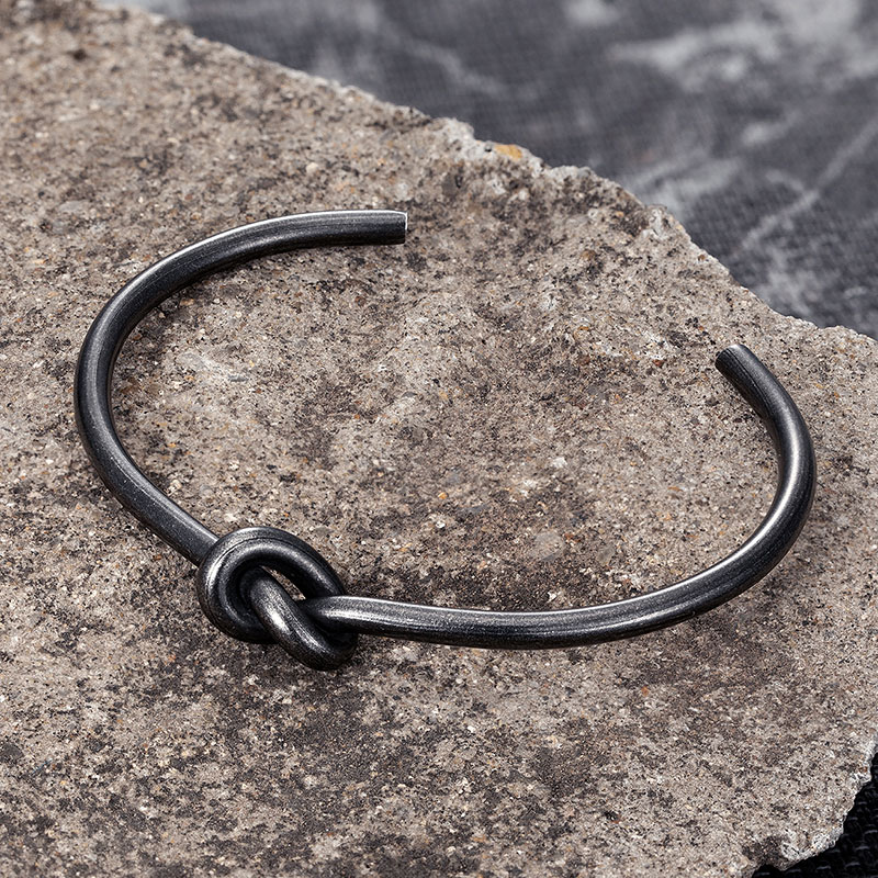 Men's stainless steel bracelet with unique knot design on a textured stone surface.