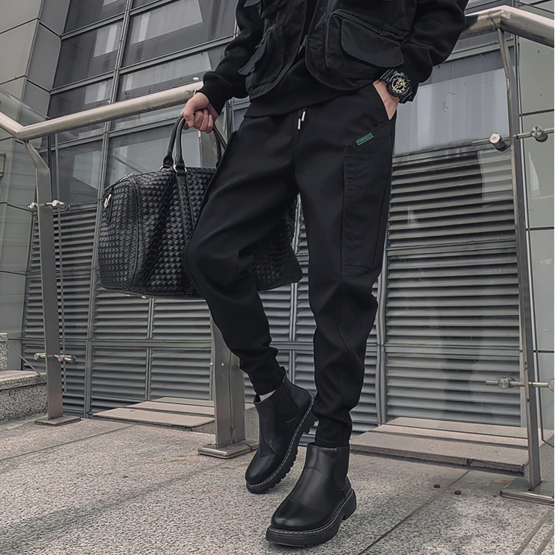 Stylish man wearing black drawstring cotton joggers, paired with trendy boots and a bag in a modern urban setting.