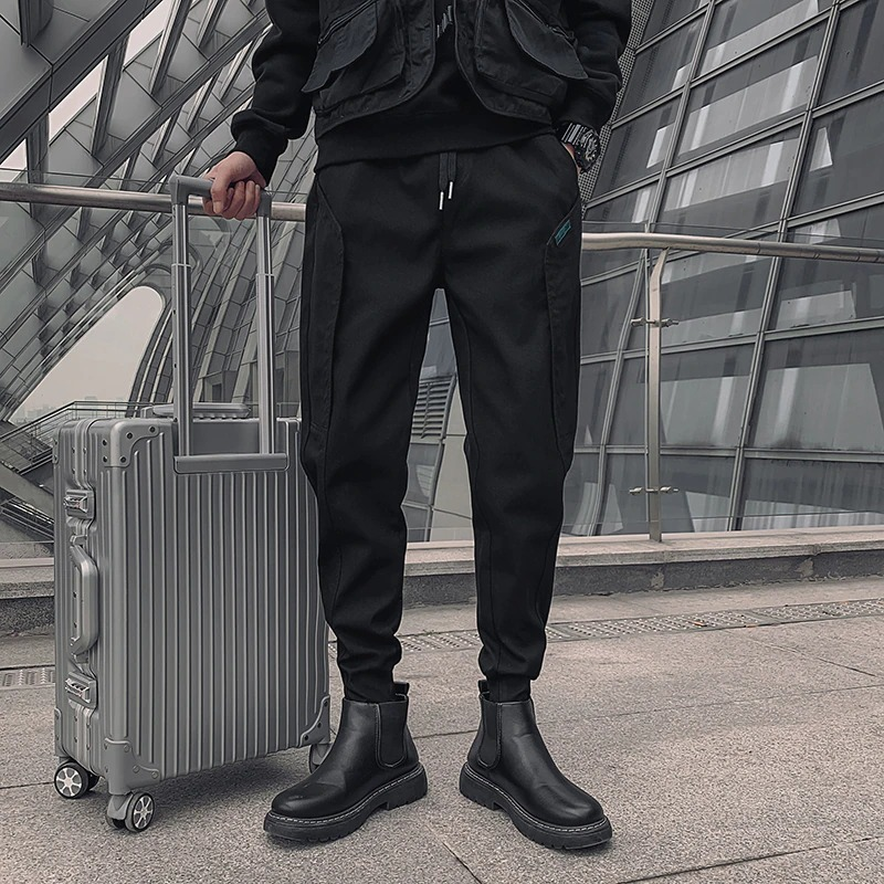 Stylish men's black cotton drawstring pants paired with sleek boots and a travel suitcase, perfect for modern casual looks.